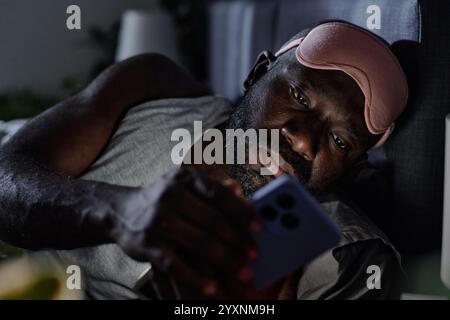 Medium close up of African American suffering from insomnia checking his social networks at night Stock Photo