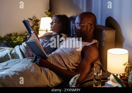 Medium close up of biracial couple lying in bed with books in hands reading stories Stock Photo