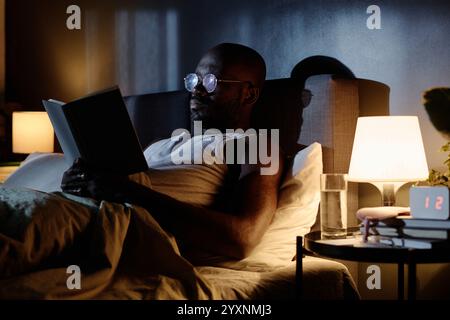 Low angle shot of African American focused on reading book at late night in bedroom Stock Photo