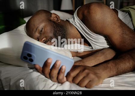 African American man lying on pillow looking at smartphones screen while checking social networks Stock Photo