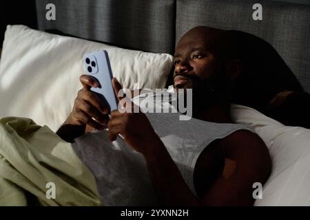High angle shot of African American man scrolling social networks while lying in bed and suffering from insomnia Stock Photo