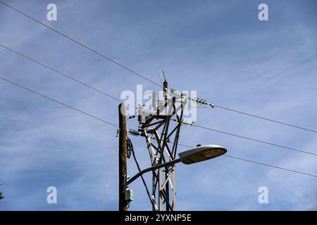 A tall power pole with a street light on top. The sky is clear and blue. The pole is surrounded by power lines Stock Photo