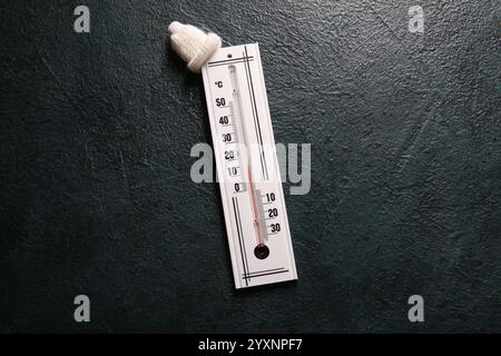 Weather thermometer with small knitted hat on dark color background Stock Photo