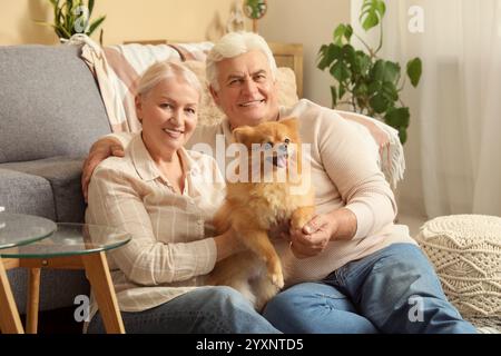 Happy senior couple with cute Pomeranian dog sitting on floor at home Stock Photo