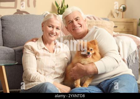 Happy senior couple with cute Pomeranian dog sitting on floor at home Stock Photo