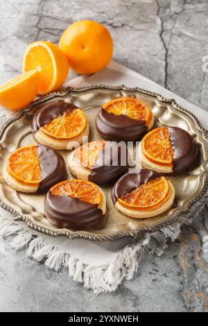 Shortbread cookies with caramelized orange covered with chocolate glaze close-up in a plate on the table. Vertical Stock Photo