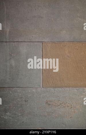 A wall made of stone with a brown and tan brick in the middle. The wall is gray and has a rough texture Stock Photo