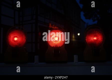 Three red lights are lit up in the dark. The lights are on a fence Stock Photo