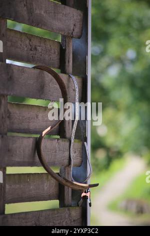 A wooden fence with a metal object hanging from it. The object is shaped like a heart and is hanging from the fence. The fence is surrounded by trees Stock Photo