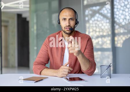 Person wearing a headset communicating via video call while working in a contemporary workspace. Related to remote work, communication, and modern technology. Stock Photo