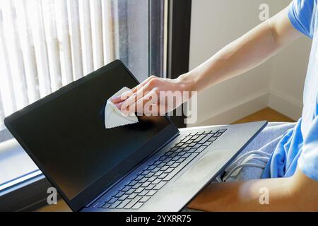 Close-up of a man's hand wiping and cleaning a laptop screen while sitting in his room Stock Photo