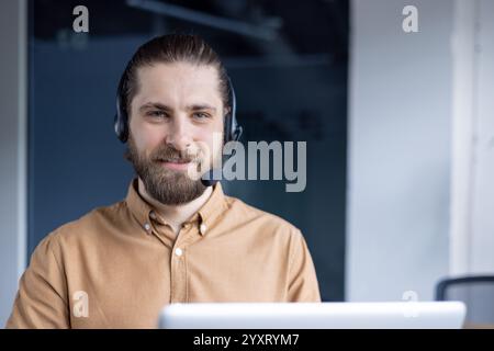A friendly customer service representative wearing a headset and smiling while working remotely from their office using modern technology for communication and assistance. Stock Photo