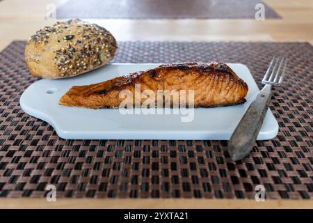flame-grilled salmon fillet with bread roll on ceramic board on table Stock Photo