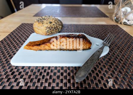 flame-grilled salmon fillet with bread roll on ceramic board on table Stock Photo