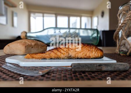 flame-grilled salmon fillet with bread roll on ceramic board on table Stock Photo