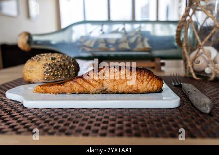 flame-grilled salmon fillet with bread roll on ceramic board on table Stock Photo