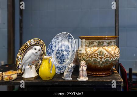 Ceramic owl statue, two figurines, yellow pitcher, plate on display at a vendor's stall at an antique market. Stock Photo