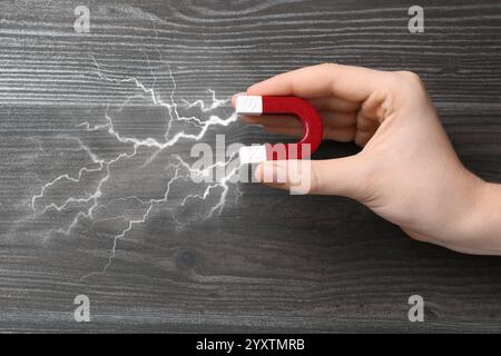Woman holding horseshoe magnet with lightnings on wooden background, top view. Space for text Stock Photo
