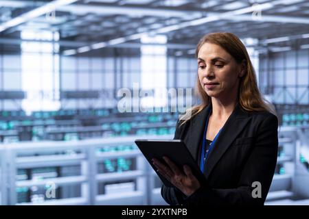 Technician in server hub checking recovery plan on tablet, monitoring energy consumption across supercomputers. Woman in data center making sure rigs are functioning optimally Stock Photo
