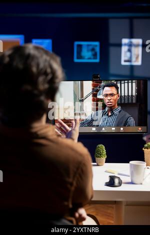 Cybersecurity expert helped by coworker during videocall to look for company security vulnerabilities and injected malware. Programmer and colleague in teleconference installing fortified code on PC Stock Photo