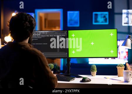 Programmer doing software debugging on green screen PC at home, checking broken lines of code displayed on monitors. IT professional in living room fixing coding problems on mockup computer Stock Photo