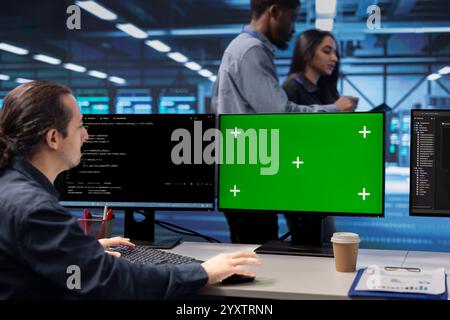 Programmer in data center using green screen computer to check for server performance issues. IT professional in server hub fixing errors slowing down hardware using mockup desktop PC Stock Photo