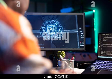 Professional male developer manages neural network at desk, working with AI code on laptop. African american IT expert freelancer developing cyber security, creating secure database. Stock Photo