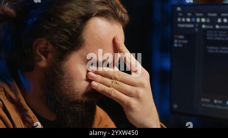 Disappointed computer scientist puzzled after being unable to remove all bugs while coding on workstation desktop. Teleworking IT specialist confused by troubling script errors, camera A close up Stock Photo
