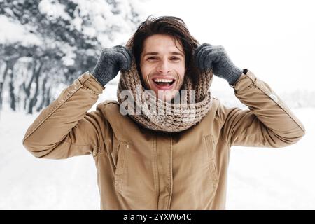 Handsome Man Pulling Scarf On Head Standing In Snowy Forest Stock Photo