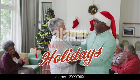 Image of happy holidays text in red over happy diverse senior couple dancing at christmas party. Christmas, holidays, festivity, tradition and celebra Stock Photo