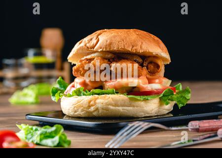 Delicious crispy fish burger with lettuce, tomato, onion ring and mayonnaise. Fish Burger with Hamburger Bun on wood background. Stock Photo