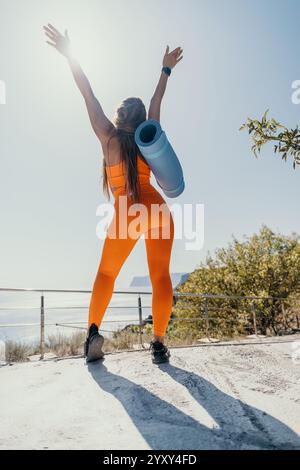 Woman in Orange Sportswear Celebrating on a Clifftop Stock Photo