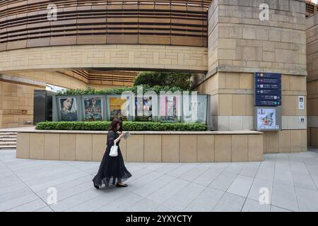Woman using mobile phone walking past movie posters in the Roppongi Hills shopping and office complex ,Tokyo, Japan, Asia. Stock Photo