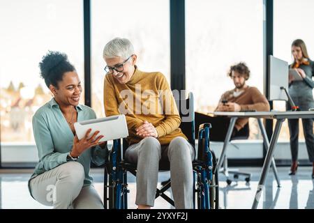 Disabled woman in wheelchair looking at computer, discussing startup project with interracial team Stock Photo