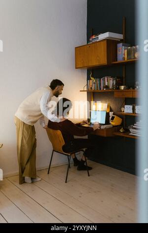 Young man with hand on shoulder of boyfriend using laptop at home Stock Photo