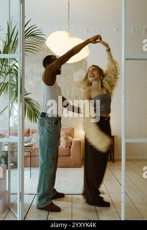 Young man in undershirt holding hands of girlfriend while dancing at home Stock Photo