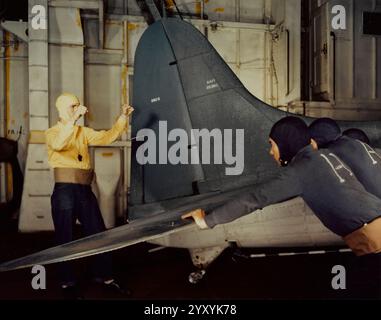 A U.S. Navy plane director (in yellow cap and jersey) guides plane handlers (blue caps and jerseys) in 'spotting' a Douglas SBD-5 Dauntless bomber (BuNo 28360) on the hangar deck of an escort carrier, circa 1943-1945 Stock Photo