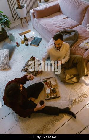 High angle view of gay couple eating snacks and drinking wine while sitting in living room at home Stock Photo
