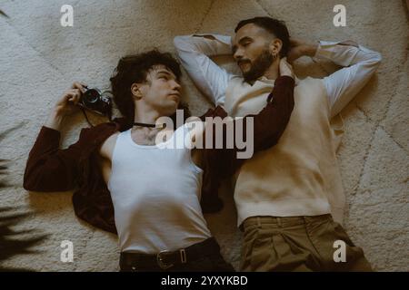 High angle view of young man holding camera and embracing boyfriend lying down on carpet at home Stock Photo