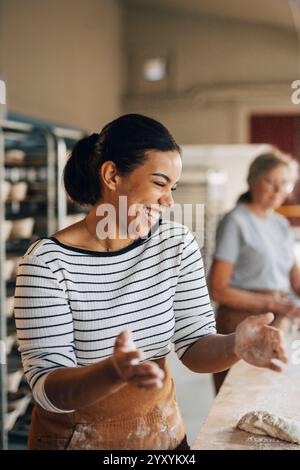 Happy female baker laughing while kneading dough at bakery Stock Photo