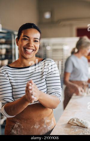 Portrait of happy female baker rubbing hands together while standing near table at bakery Stock Photo