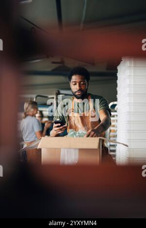 Male baker wearing apron and taking inventory of supplies in cardboard box at home Stock Photo