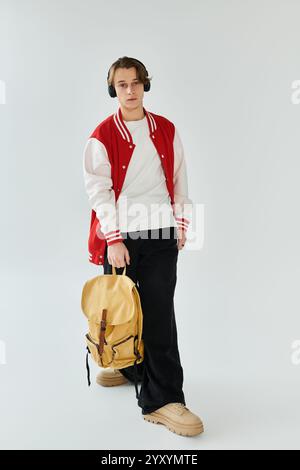 A handsome young man stands confidently in a studio, wearing a stylish bomber jacket and headphones. Stock Photo