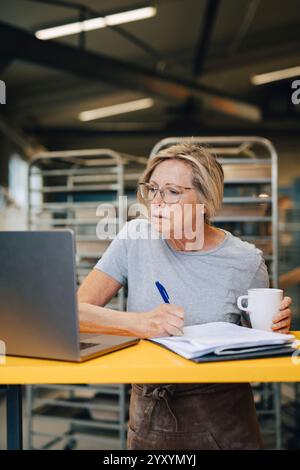 Focused senior female entrepreneur taking down notes while working at bakery Stock Photo
