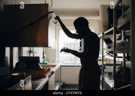 Silhouette of male baker washing dishes while working in commercial kitchen Stock Photo