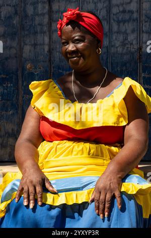 A Palenquera Woman Sitting On Stone Steps Wearing A Bright Dress in Cartagena, Colombia Stock Photo