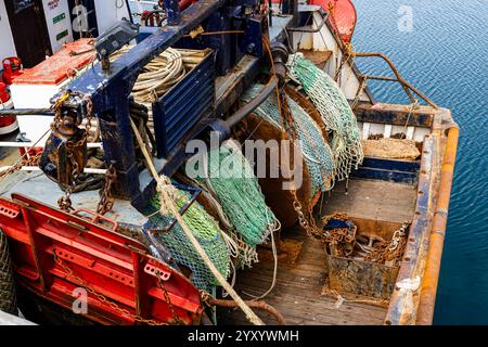 stern end of a fishing trawler with the nets stowed alongside a harbour wall Stock Photo