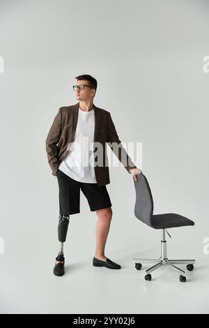 A young handsome man in a blazer stands next to a chair, showcasing his prosthetic leg. Stock Photo