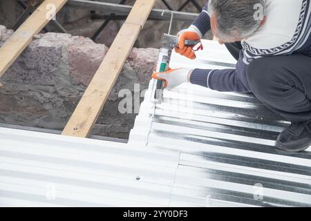Worker using glue gun with adhesive to fix the metal steel on the roof. Stock Photo