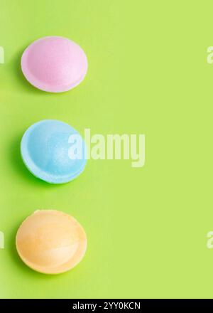 Colorful flying saucer candy in pink, blue, and yellow are aligned vertically on a green background, showcasing vibrant and playful confectionery in a Stock Photo